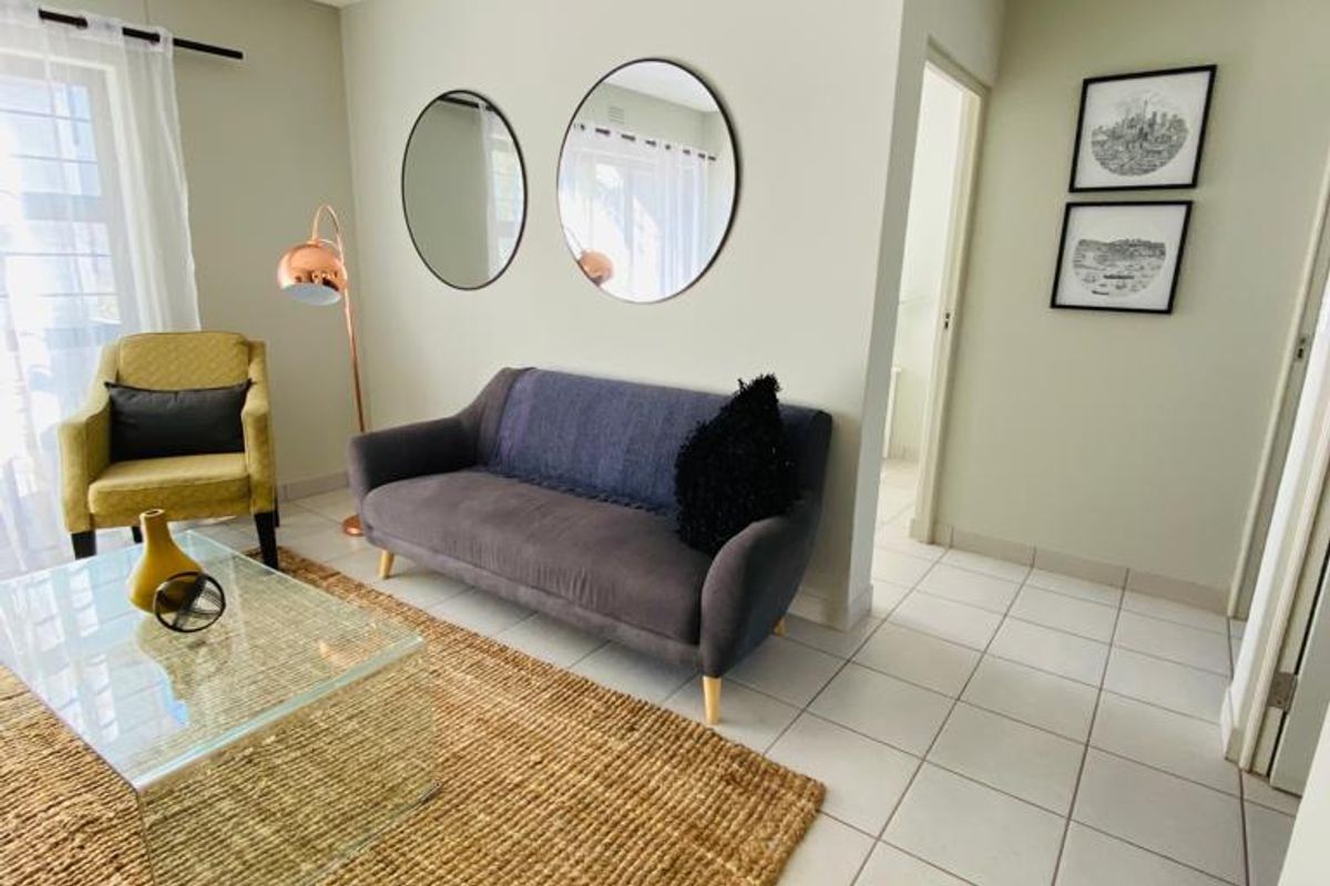 A bright and well-maintained living room featuring neutral tiled flooring and a classic tongue and groove ceiling.