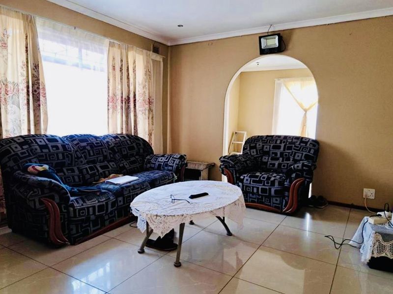A living room featuring tiled flooring, an arched doorway leading to an adjacent space, and a large window allowing natural light.