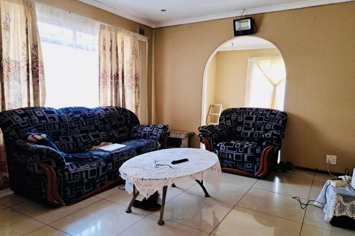 A living room featuring tiled flooring, an arched doorway leading to an adjacent space, and a large window allowing natural light.