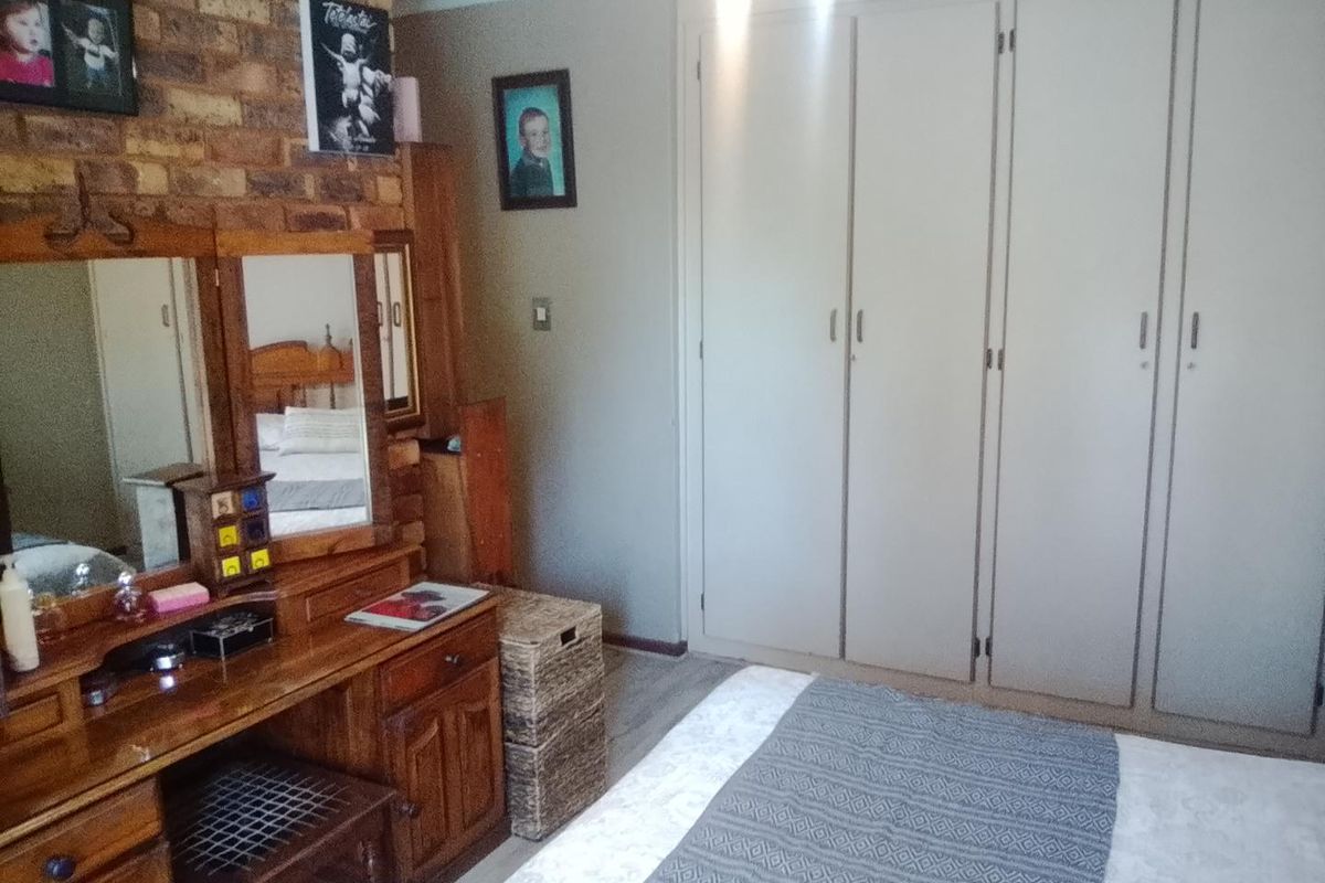 A bedroom featuring a prominent exposed brick wall, neutral painted walls, and ample built-in cupboard storage with laminate flooring.