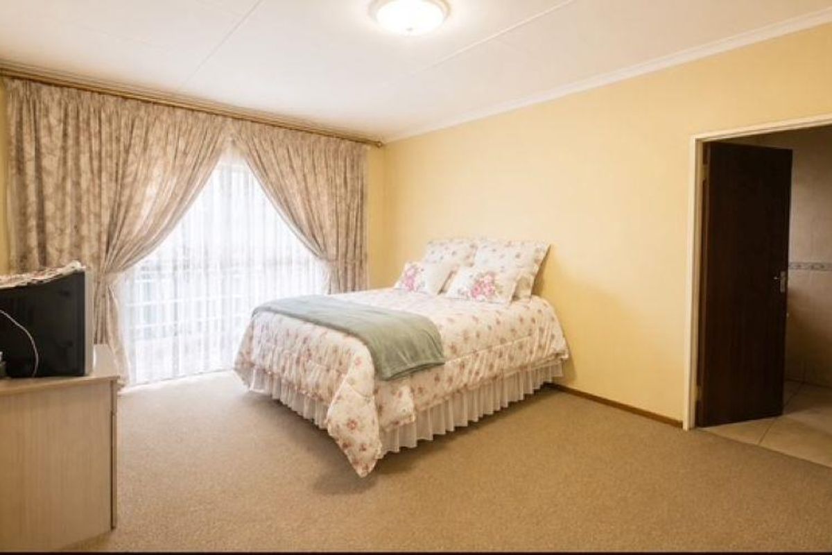 A spacious bedroom featuring neutral wall tones, carpeted flooring, and direct access to an en-suite bathroom.