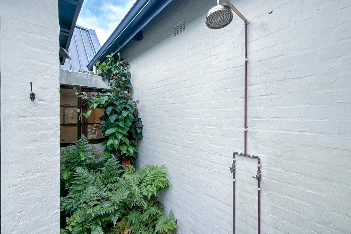 An outdoor shower area featuring exposed copper piping mounted on a painted brick wall, set within a private, landscaped courtyard space.