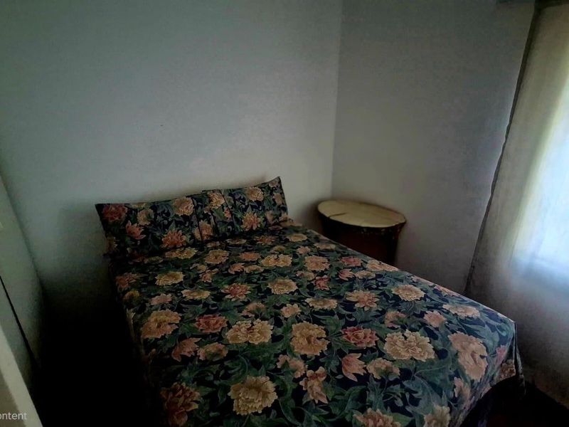 A compact bedroom featuring a built-in cupboard and natural light from a side window, requiring cosmetic updates to improve the overall finish.