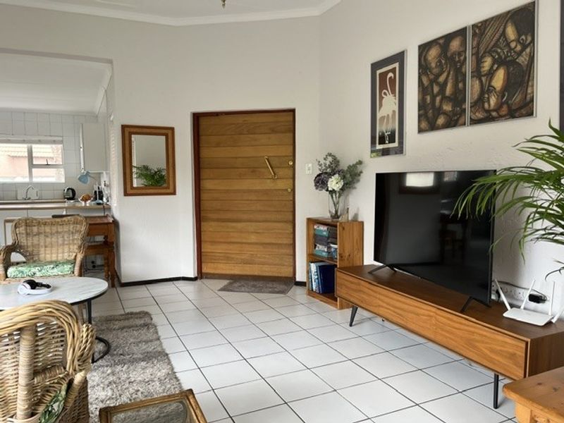 Open plan living area featuring tiled flooring and a timber entrance door, with an adjacent kitchen space visible in the background.