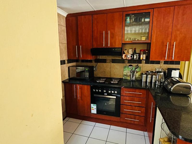 A compact kitchen featuring warm-toned wooden cabinetry, granite countertops, built-in oven and hob, and tiled flooring.