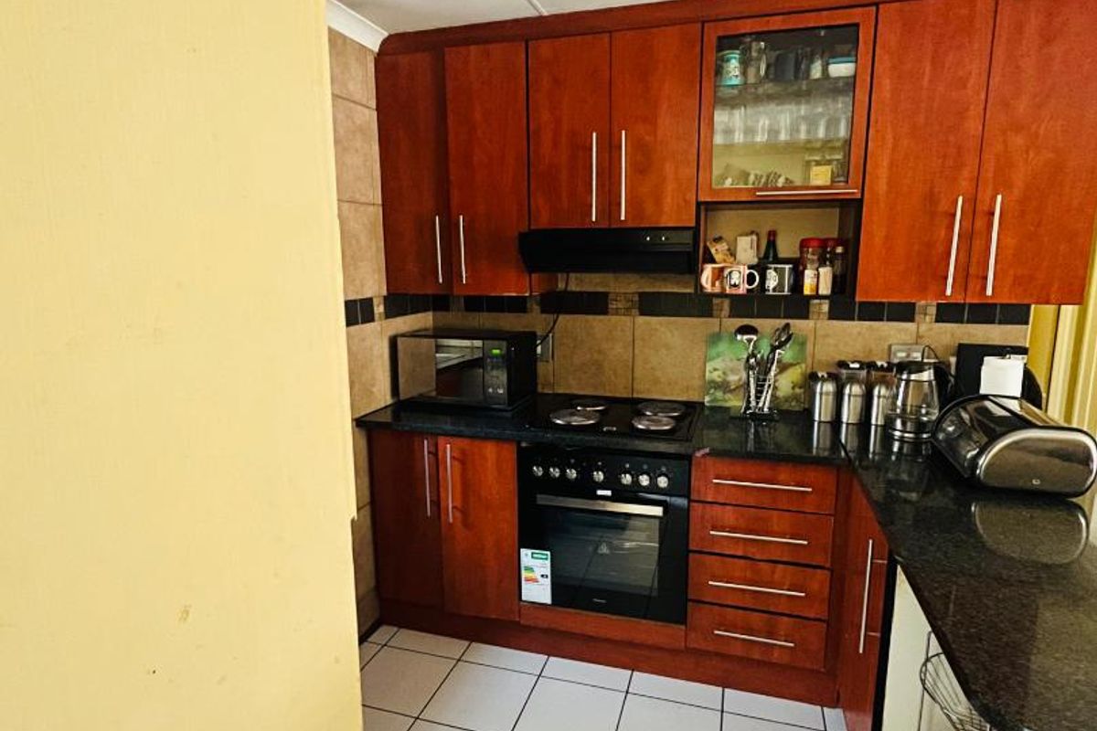 A compact kitchen featuring warm-toned wooden cabinetry, granite countertops, built-in oven and hob, and tiled flooring.