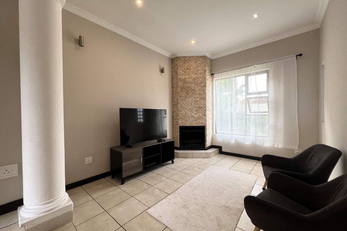 A cozy living room featuring a corner fireplace with stone cladding, tiled flooring, recessed ceiling lighting, and a decorative structural column.
