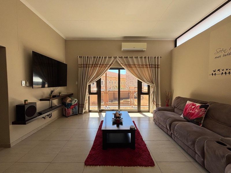 A well-maintained living room featuring tiled flooring, a split-system air conditioner, and a sliding glass door providing access to an outdoor balcony area.