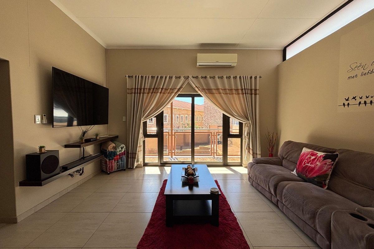 A well-maintained living room featuring tiled flooring, a split-system air conditioner, and a sliding glass door providing access to an outdoor balcony area.