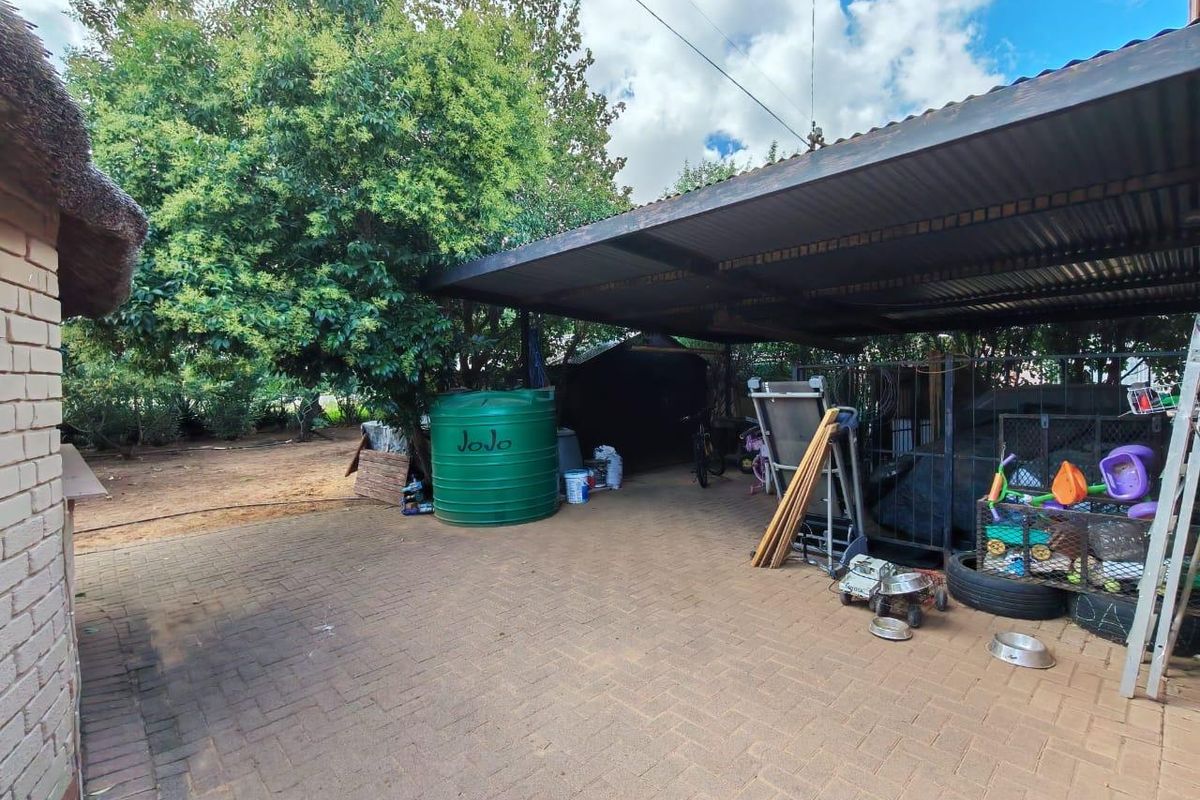 Outdoor area featuring a covered carport structure, paved flooring, and a large water storage tank set within a garden space.