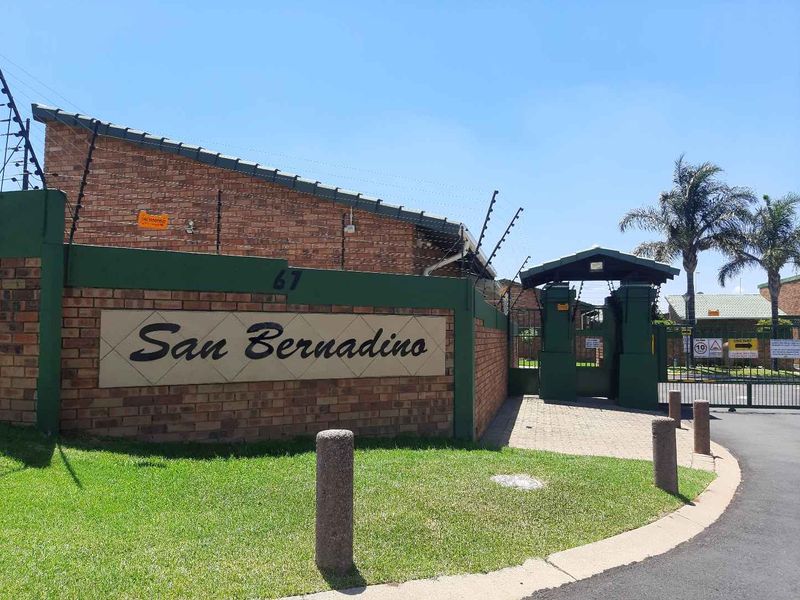 Front entrance view of San Bernadino cluster complex featuring a brick boundary wall, electric fencing, and a secure gated access point.