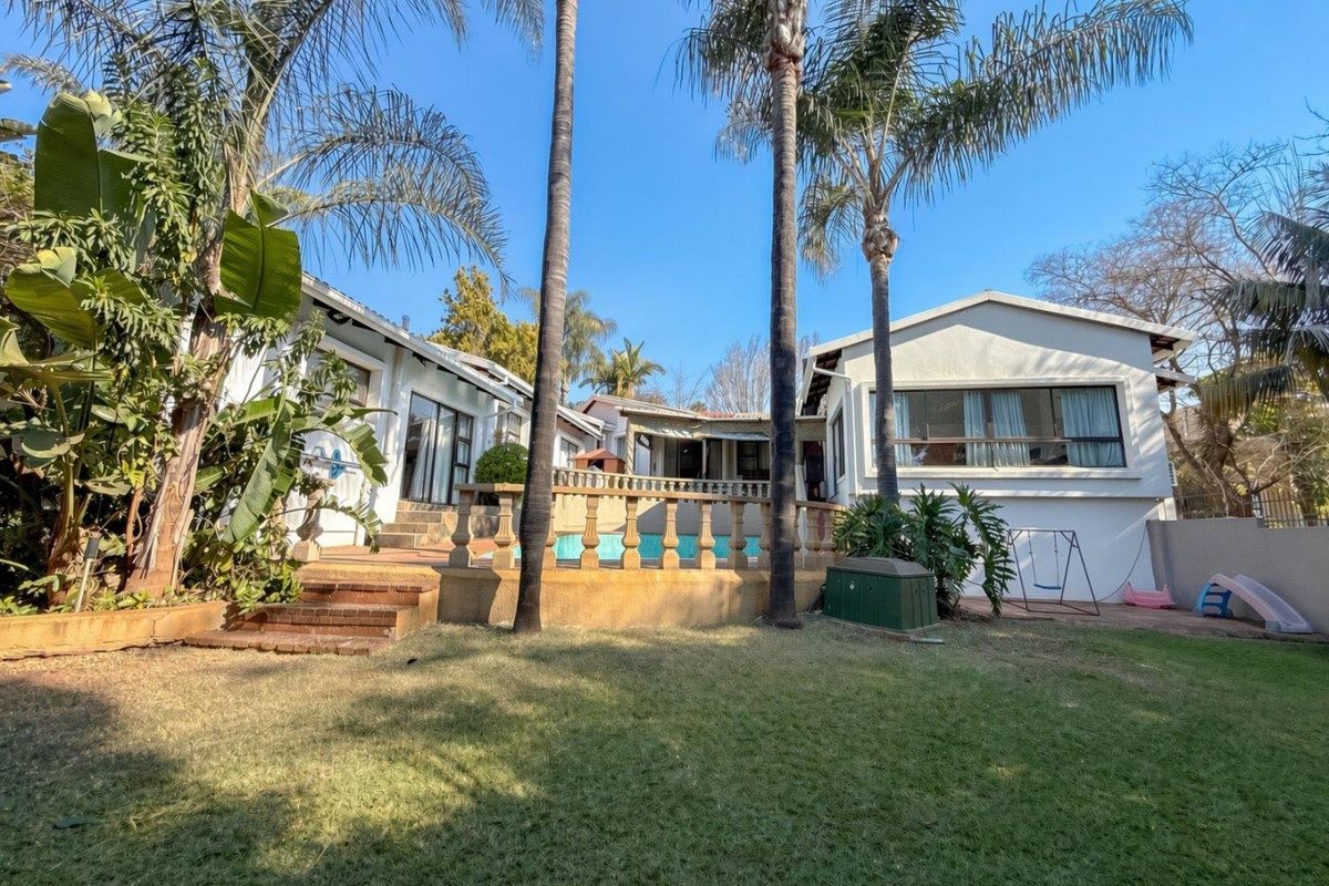 Rear view of the property featuring a swimming pool, raised patio area with balustrade, and established garden with mature palm trees.