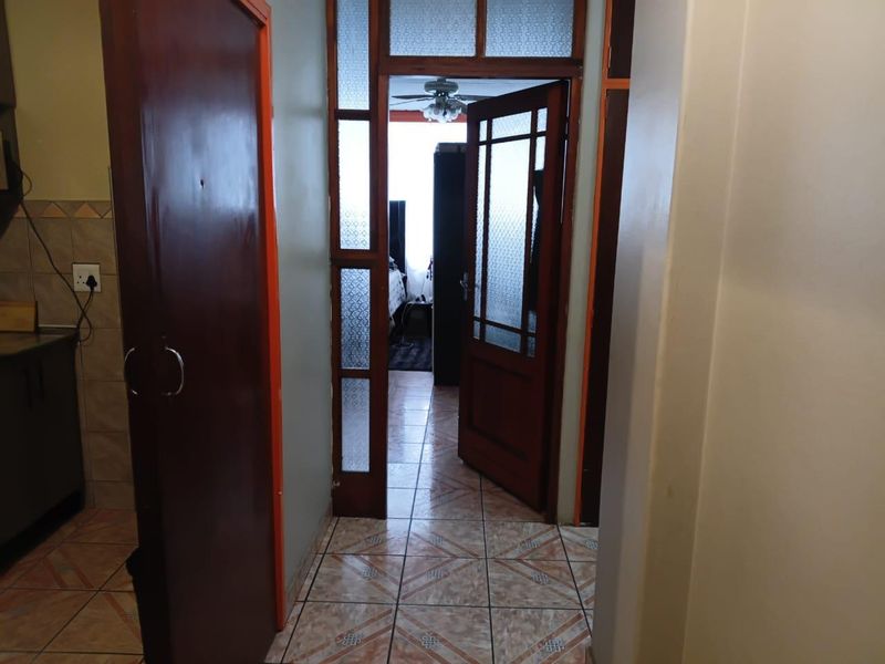 A functional hallway featuring tiled flooring and timber-framed glass doors, providing access to adjacent living spaces within the apartment.