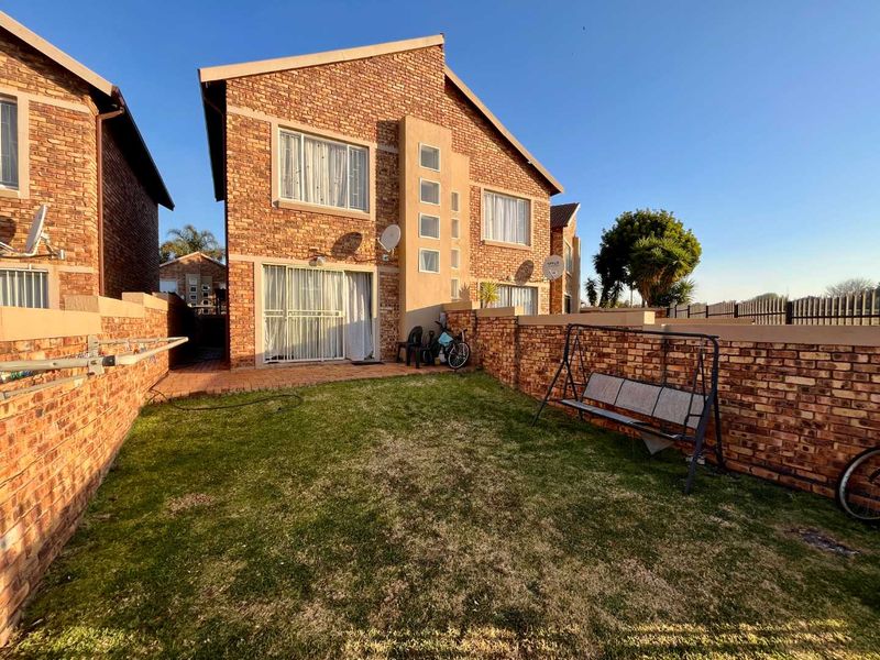 Rear view of a face brick townhouse featuring a private garden, paved patio area, and glass sliding door access.