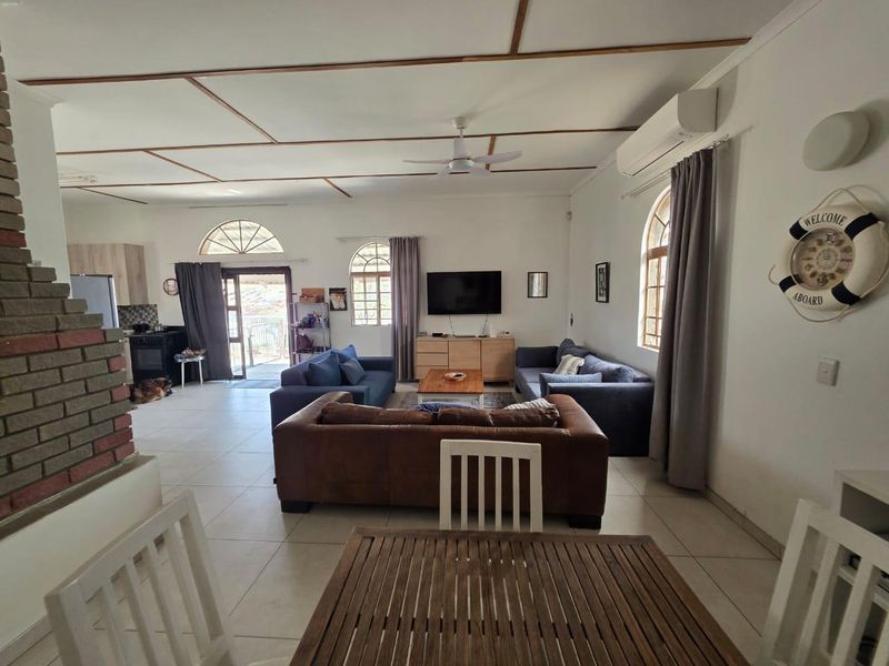 Spacious open-plan living area featuring tiled floors, a brick fireplace, ceiling fan, and split-system air conditioning with access to an outdoor patio.