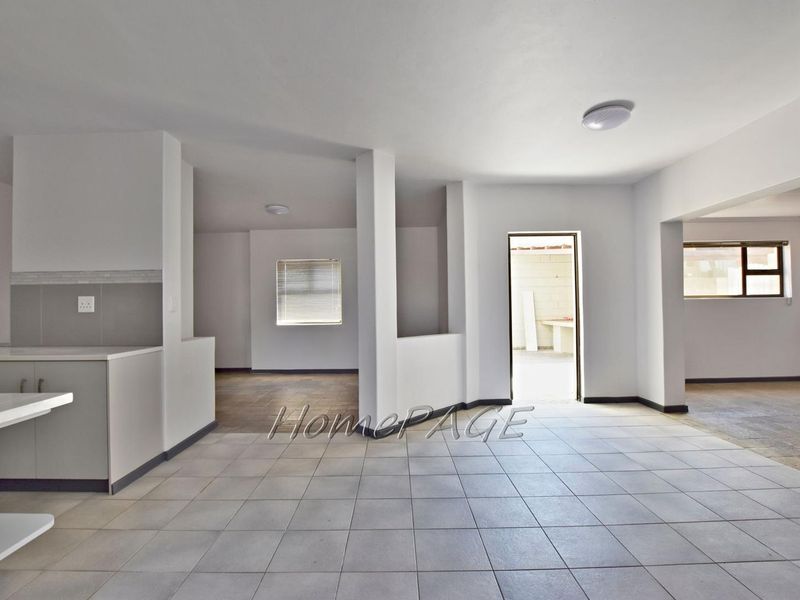 Spacious open-plan living and kitchen area featuring neutral tiled flooring, clean white walls, and ample natural light throughout the interconnected living spaces.