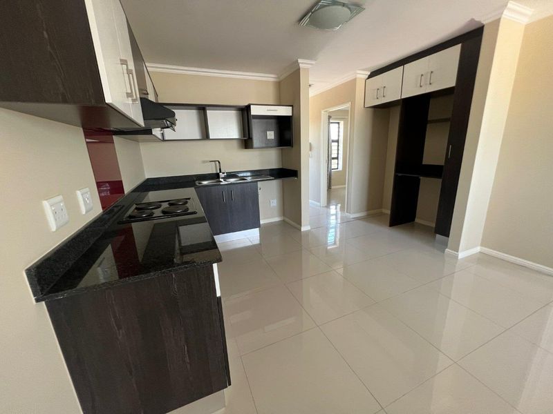 Modern kitchen featuring dark wood cabinetry, granite countertops, integrated hob, extractor fan, and polished tiled flooring in an open-plan layout.