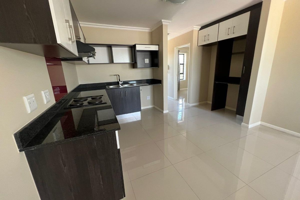Modern kitchen featuring dark wood cabinetry, granite countertops, integrated hob, extractor fan, and polished tiled flooring in an open-plan layout.
