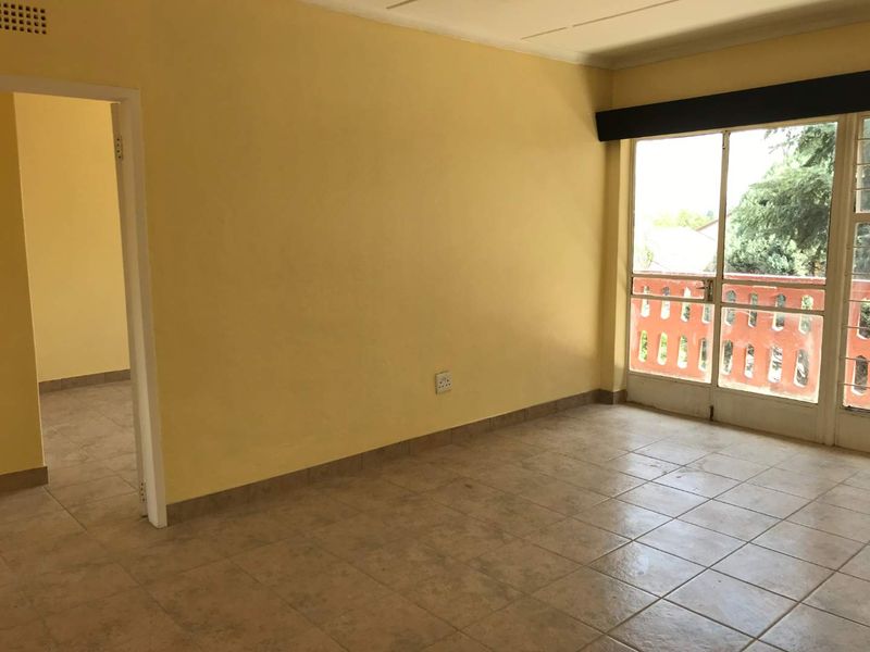 An empty living room featuring tiled flooring, yellow walls, and a sliding glass door leading to a balcony area.