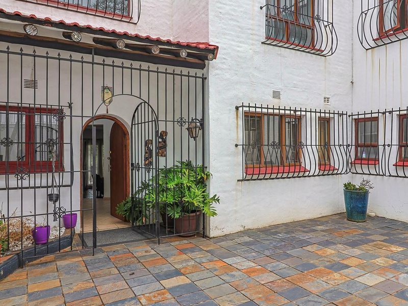 A paved rear courtyard area featuring wrought iron security gates and window bars, with access to the main dwelling.