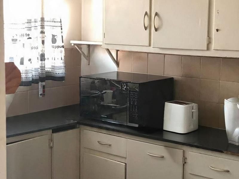 A compact kitchen featuring dated built-in cabinetry, dark laminate countertops, and a tiled backsplash, offering potential for a modern renovation.