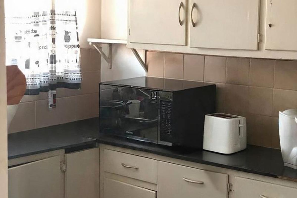 A compact kitchen featuring dated built-in cabinetry, dark laminate countertops, and a tiled backsplash, offering potential for a modern renovation.