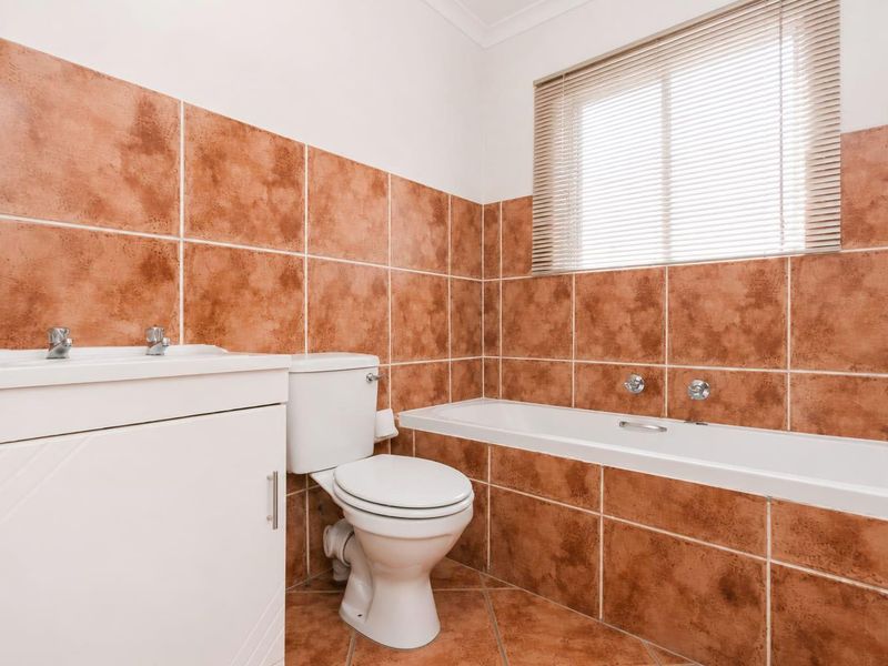 A functional bathroom featuring a bathtub, vanity basin, and toilet, finished with terracotta-style wall and floor tiling.