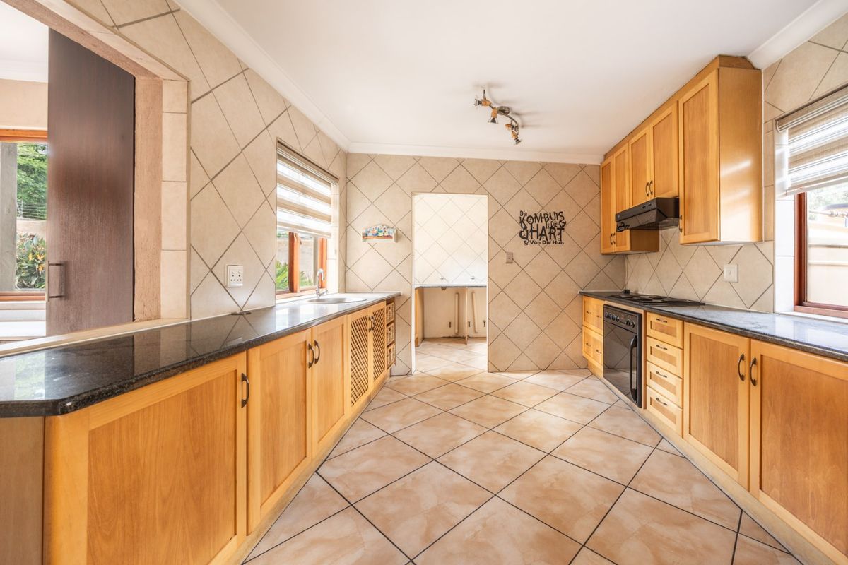 A functional kitchen featuring wooden cabinetry, granite countertops, built-in oven, hob, and extractor fan, with tiled flooring and backsplash throughout.