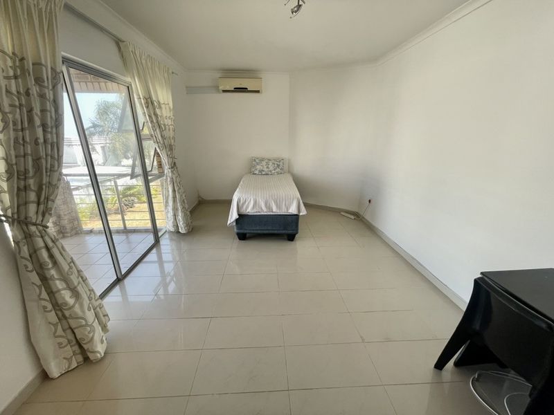 A spacious bedroom featuring neutral tiled flooring, a wall-mounted air conditioning unit, and large sliding glass doors providing access to the outdoor area.
