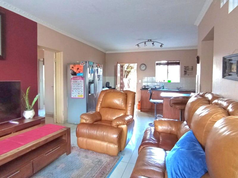 Open-plan living area featuring a combined lounge and kitchen space with tiled flooring, neutral walls, and a functional breakfast counter layout.
