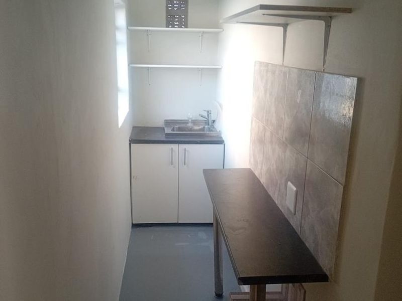 A compact scullery or utility area featuring built-in cabinetry, a stainless steel sink, tiled splashback, and fixed shelving for efficient storage and prep.