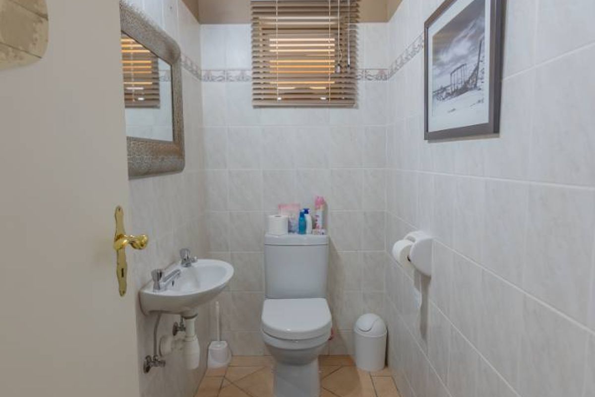 A compact guest bathroom featuring ceramic wall and floor tiles, a wall-mounted basin, and a distinctive timber-clad ceiling.
