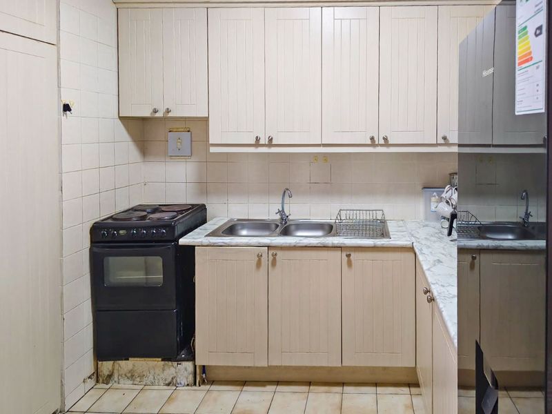 A functional kitchen featuring cream-colored cabinetry, marble-effect countertops, a double sink, and tiled finishes, offering potential for cosmetic updates.
