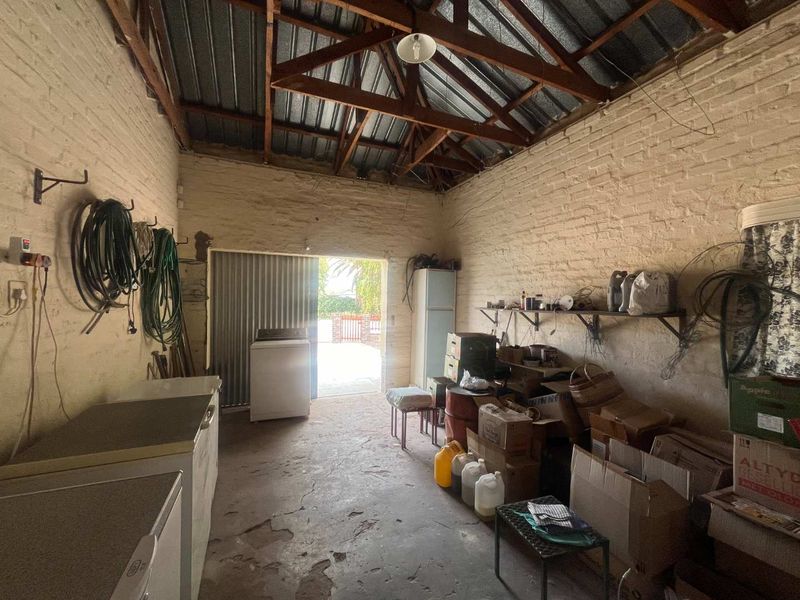 A rustic utility space featuring exposed timber roof trusses, painted brick walls, and a concrete floor, offering potential for storage or workshop conversion.