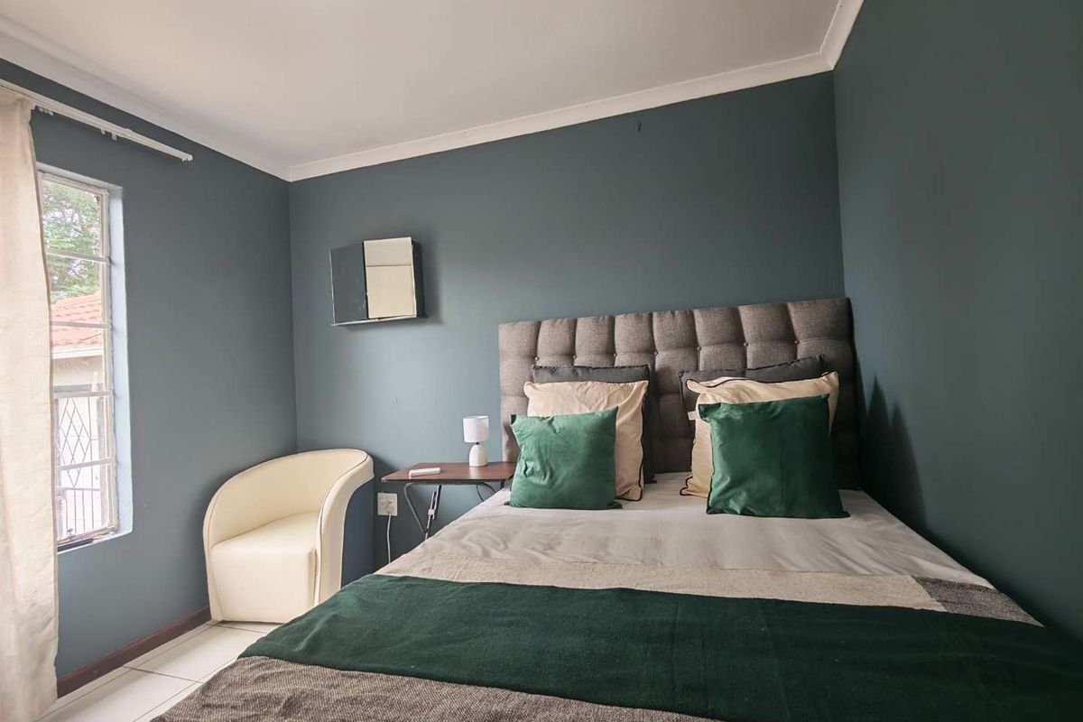A well-maintained bedroom featuring dark blue accent walls, tiled flooring, and a window with security bars.