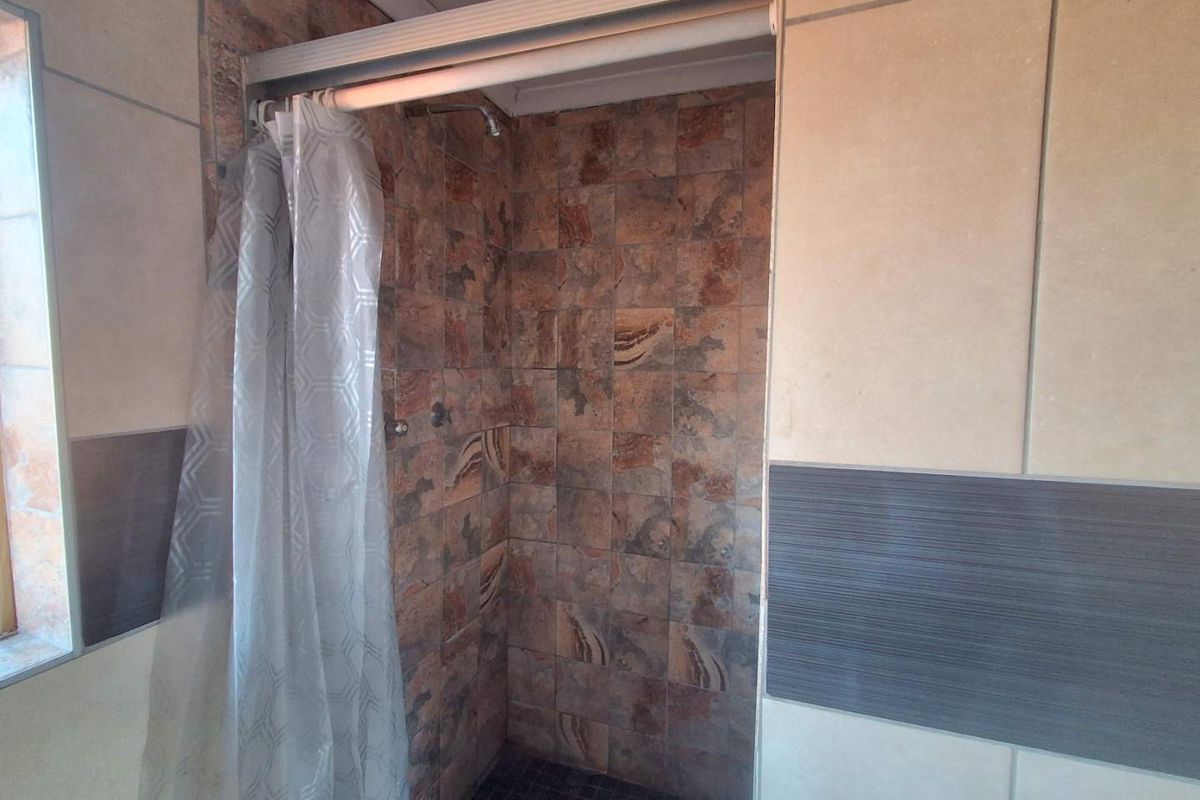 A shower enclosure featuring textured stone-look wall tiles, a dark mosaic floor, and a sliding shower curtain rail.