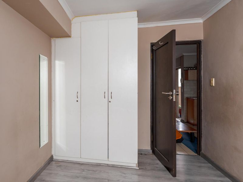 A vacant bedroom featuring built-in white wardrobes, laminate flooring, and neutral wall tones, offering a blank canvas for personalization.