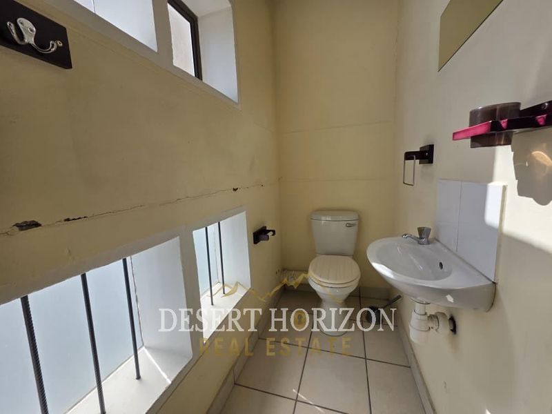 A compact bathroom featuring a wall-mounted sink, toilet, and tiled flooring, currently showing signs of wear and requiring cosmetic maintenance.