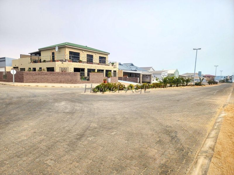 Street view of a multi-story residential property featuring stone cladding, a brick boundary wall, and an upper-level balcony.