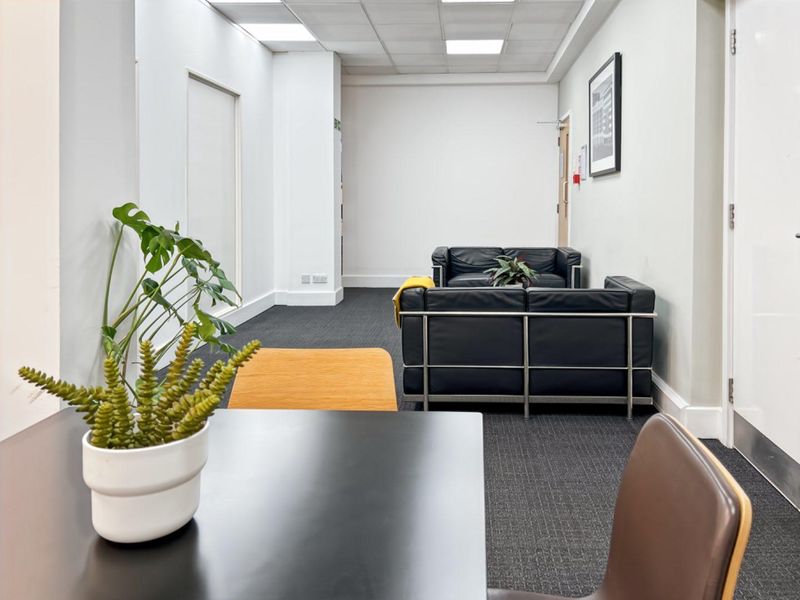 A professional office space featuring a suspended ceiling, recessed lighting, and dark carpet flooring, providing a clean and functional work environment.