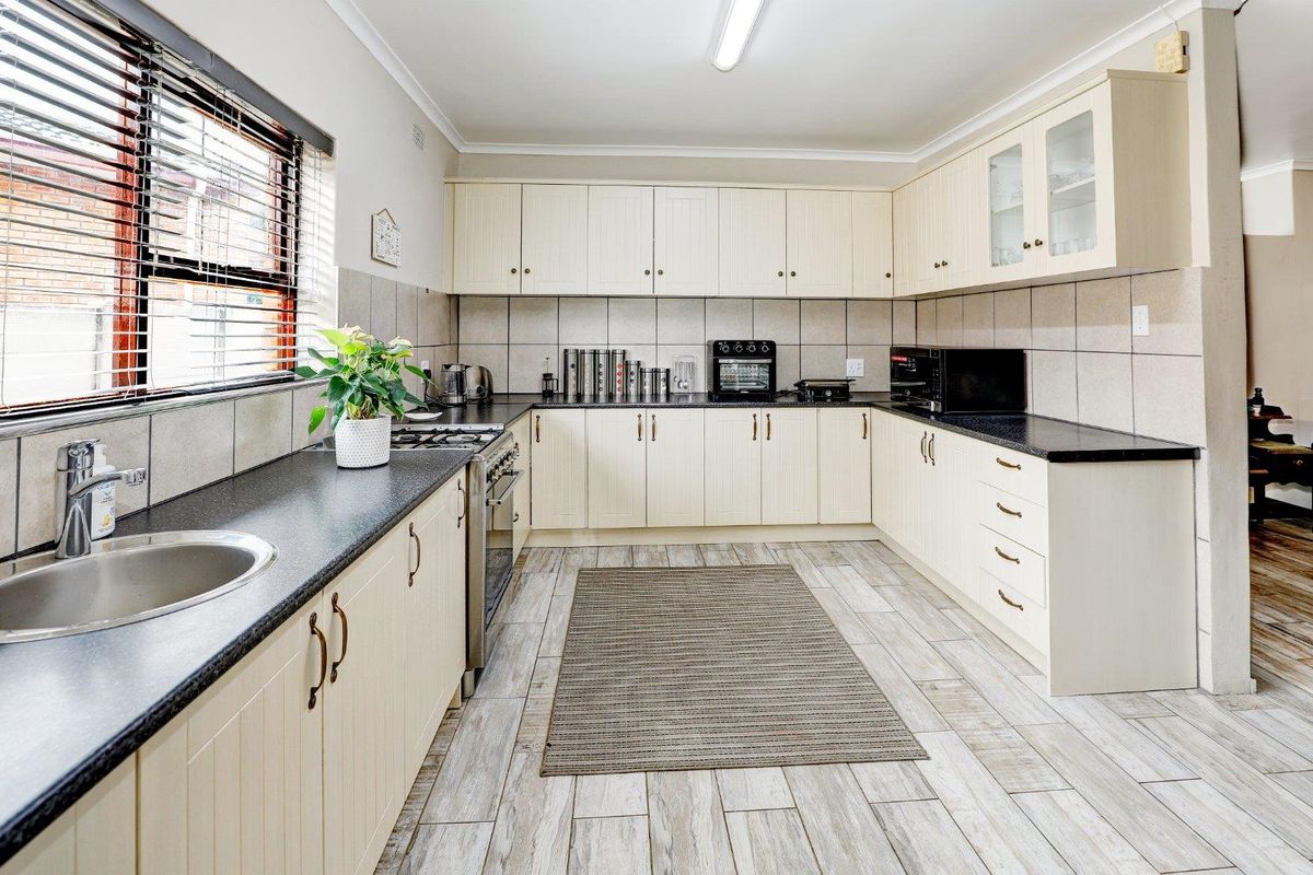 A functional kitchen featuring cream cabinetry, dark countertops, tiled splashbacks, and light-toned wood-look floor tiles.
