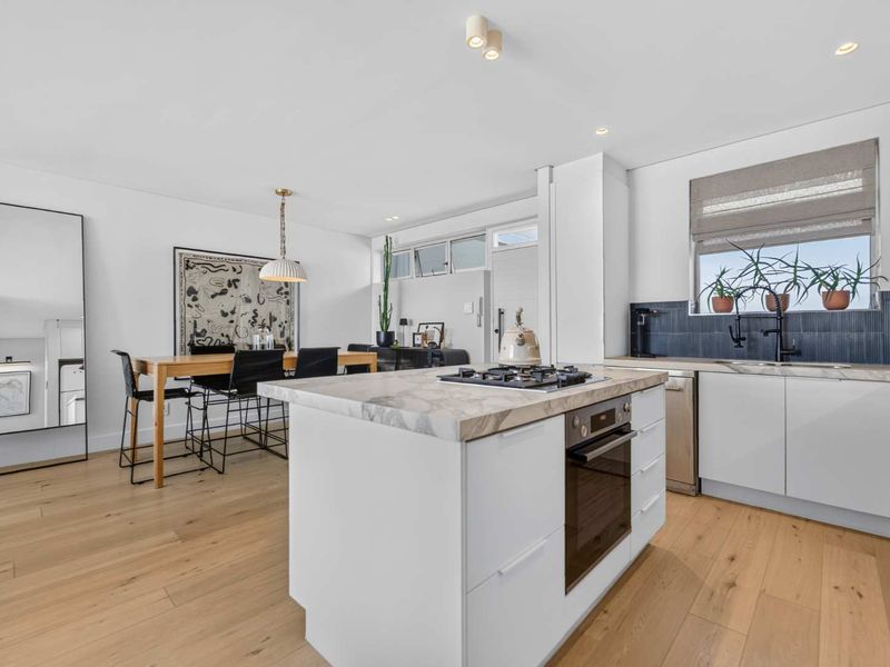 Modern open-plan kitchen and dining area featuring a central island with gas cooktop, stone countertops, and high-quality hardwood flooring throughout.