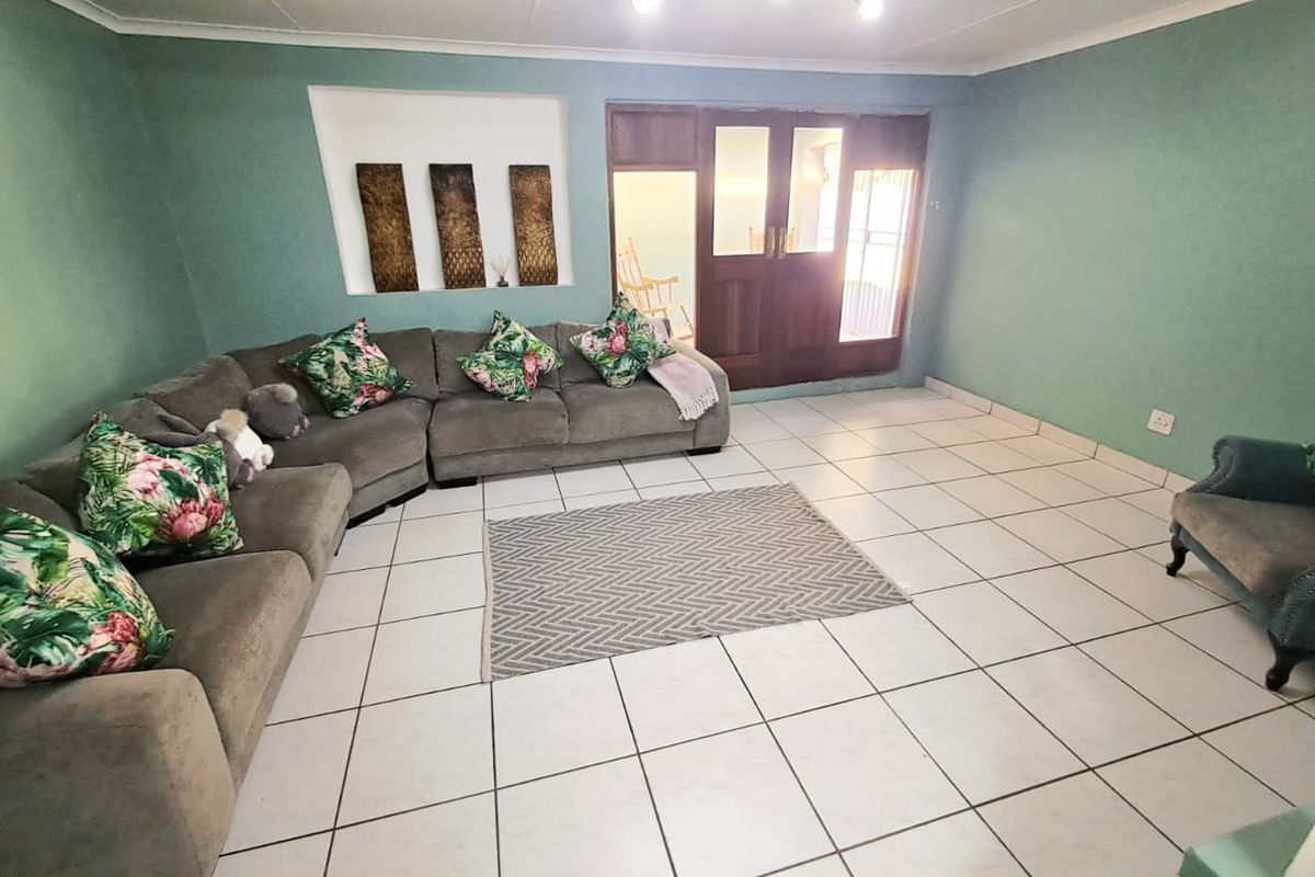 A spacious living room featuring light-colored floor tiles, a recessed wall niche, and a wooden door leading to an adjacent area.