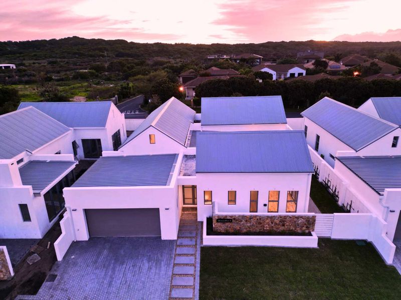 Aerial view of a modern residential property featuring a corrugated metal roof, double garage, and stone-clad entrance wall at sunset.