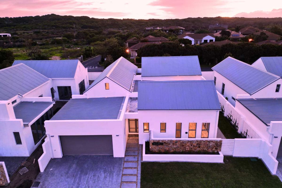 Aerial view of a modern residential property featuring a corrugated metal roof, double garage, and stone-clad entrance wall at sunset.