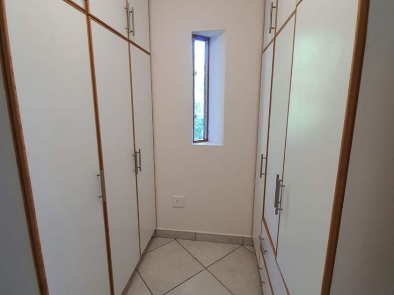 A functional utility or storage space featuring extensive built-in cabinetry, tiled flooring, and a narrow vertical window for natural light.