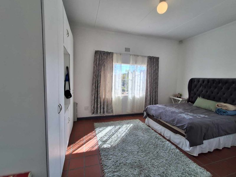 A spacious bedroom featuring built-in cupboards, tiled flooring, and natural light through a window fitted with security bars.