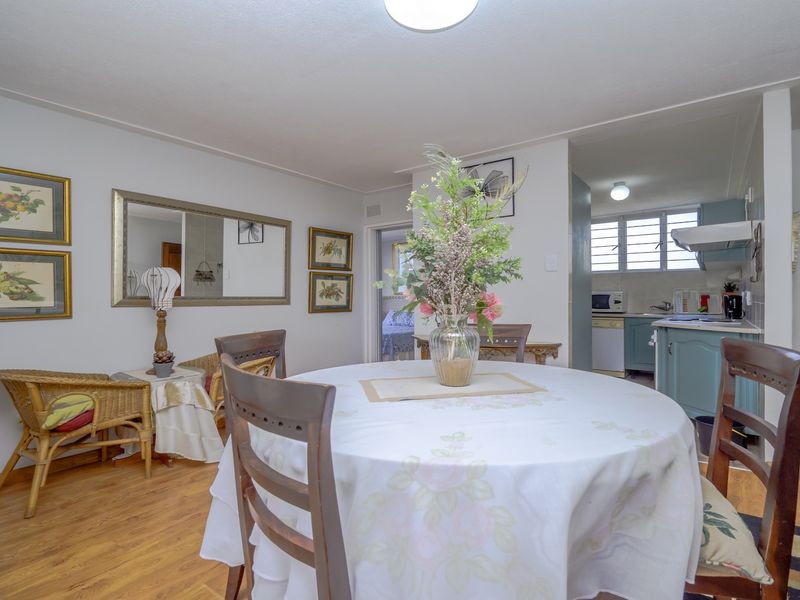 Open plan dining area featuring laminate flooring, flowing into a functional kitchen space with cabinetry and louvered windows.