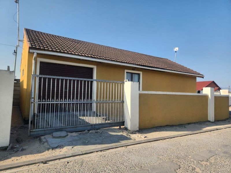 Front elevation of a single-story house featuring a garage, secure metal gate, and perimeter walling.