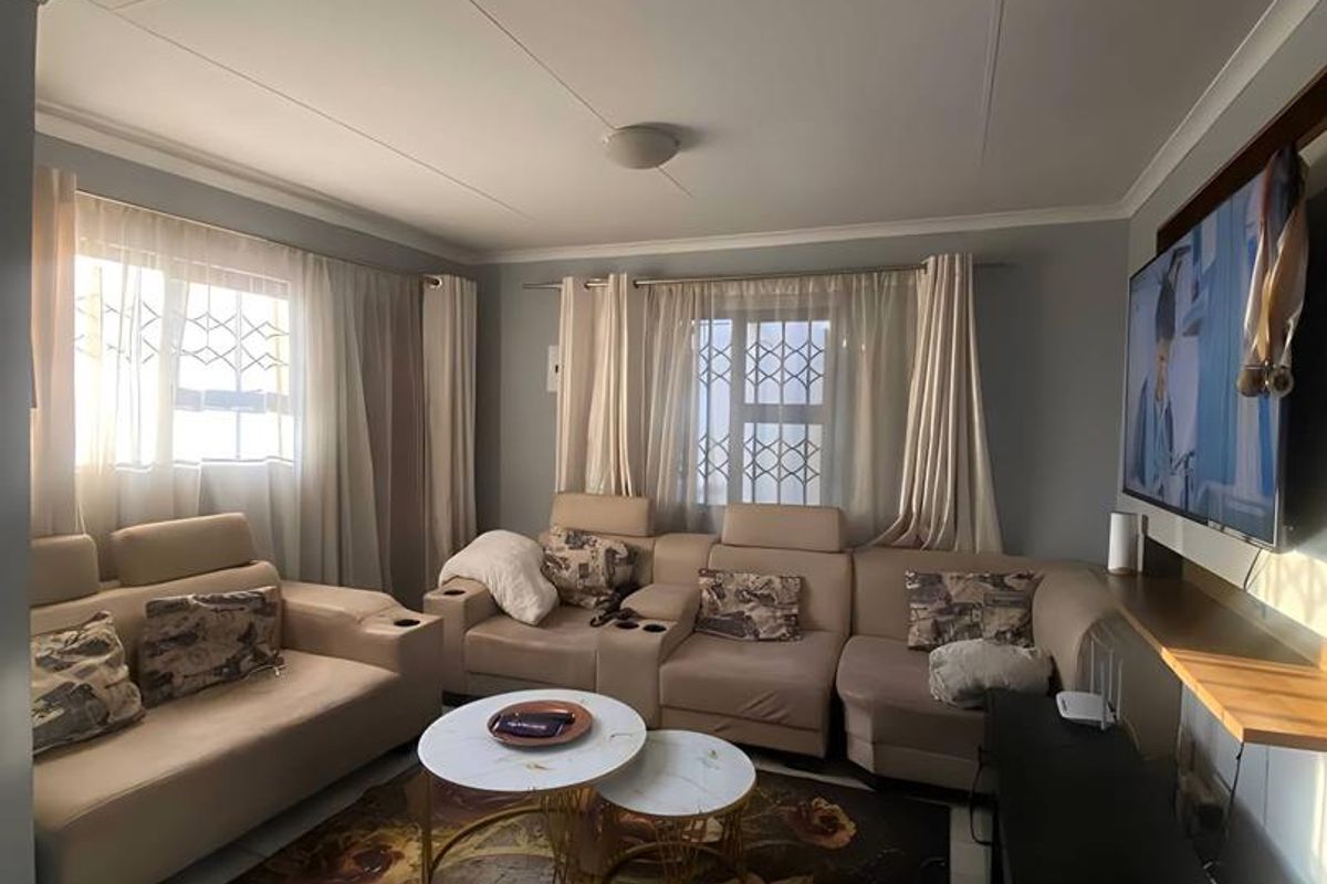 A comfortable living room featuring tiled flooring, neutral wall tones, and security bars on the windows, providing a functional and well-lit space.